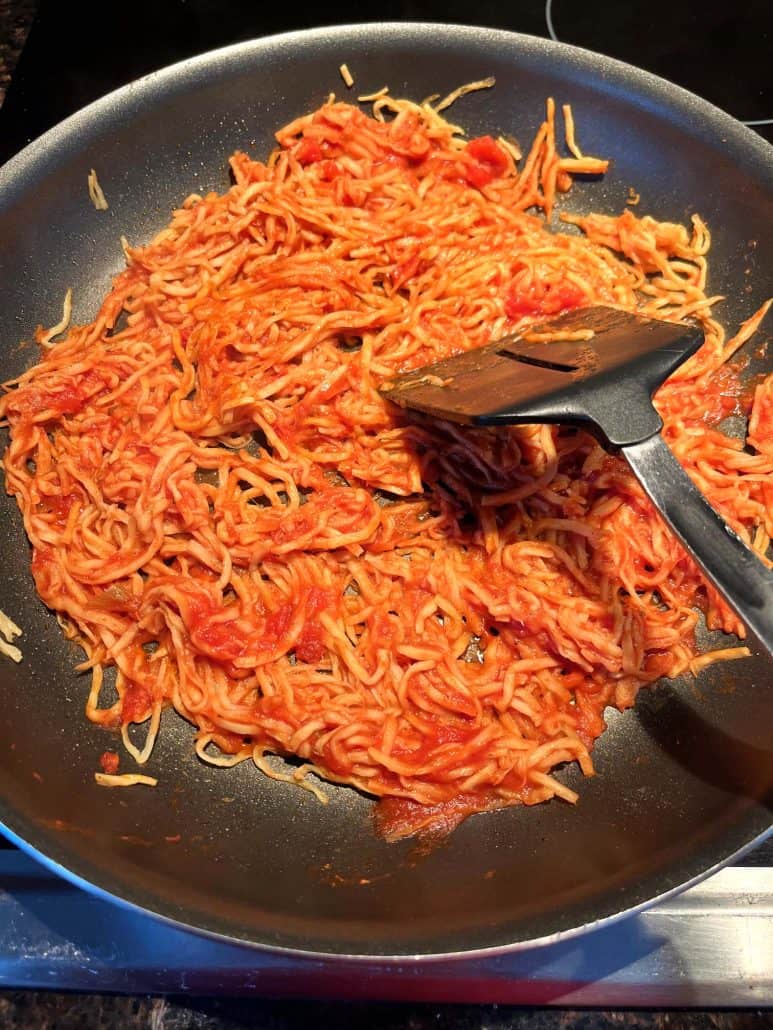 A spatula stirring hearts of palm pasta in marinara sauce on a stovetop.