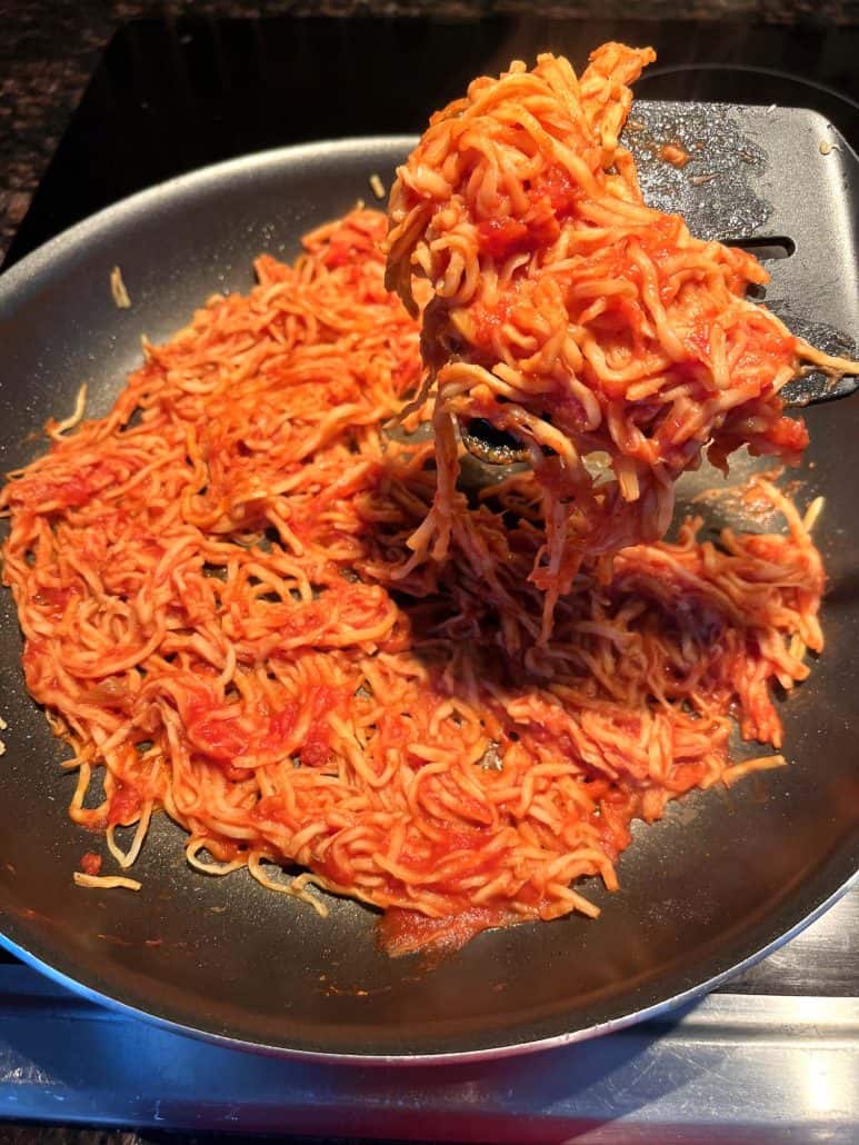 A spatula lifting hearts of palm pasta coated in marinara sauce from a frying pan, showcasing its texture and how easily it cooks into a tasty, low-carb meal.