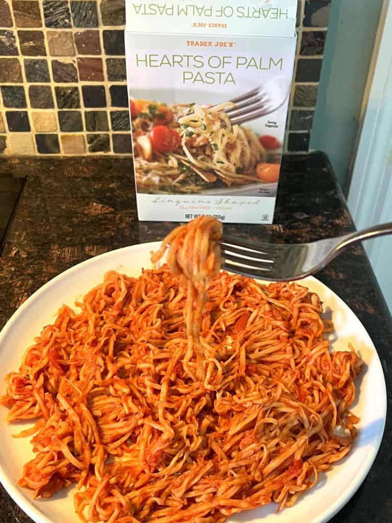 Plate of cooked Trader Joe’s Hearts of Palm Pasta with marinara sauce, served with a fork, with the product packaging in the background. A healthy, low-carb pasta alternative ready to enjoy!