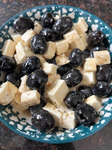 A bowl of marinated olives and feta cheese, coated in Italian dressing—an easy and flavorful appetizer perfect for parties or snacking.
