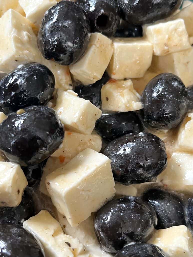 A close-up of marinated black olives and feta cheese, coated in Italian dressing for a flavorful and easy appetizer.