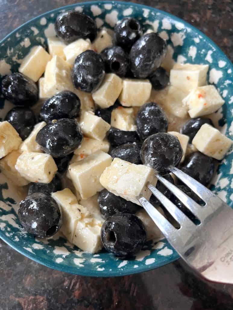 A fork scooping up a no-cook, marinated olives and feta cheese.