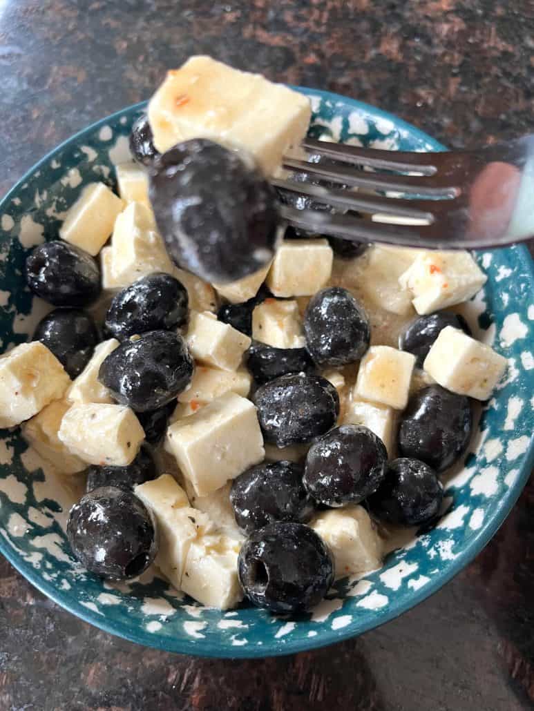 A fork holding a bite of marinated olives and feta cheese, showcasing this easy and flavorful appetizer.