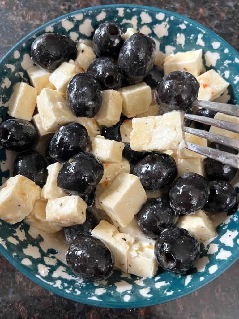 A fork picking up marinated olives and feta cheese from a bowl, highlighting this simple and delicious appetizer.