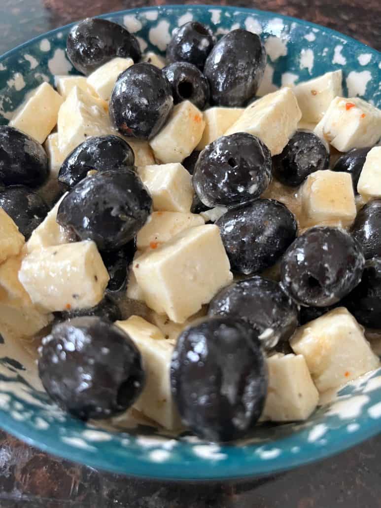A bowl of marinated black olives and cubed feta cheese, tossed in flavorful Italian dressing.