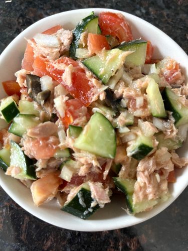Fresh Mediterranean Tuna Salad in a white bowl with chopped tomatoes, cucumbers, olives, and tuna, dressed with olive oil and lime juice—perfect for a healthy, no-mayo meal.