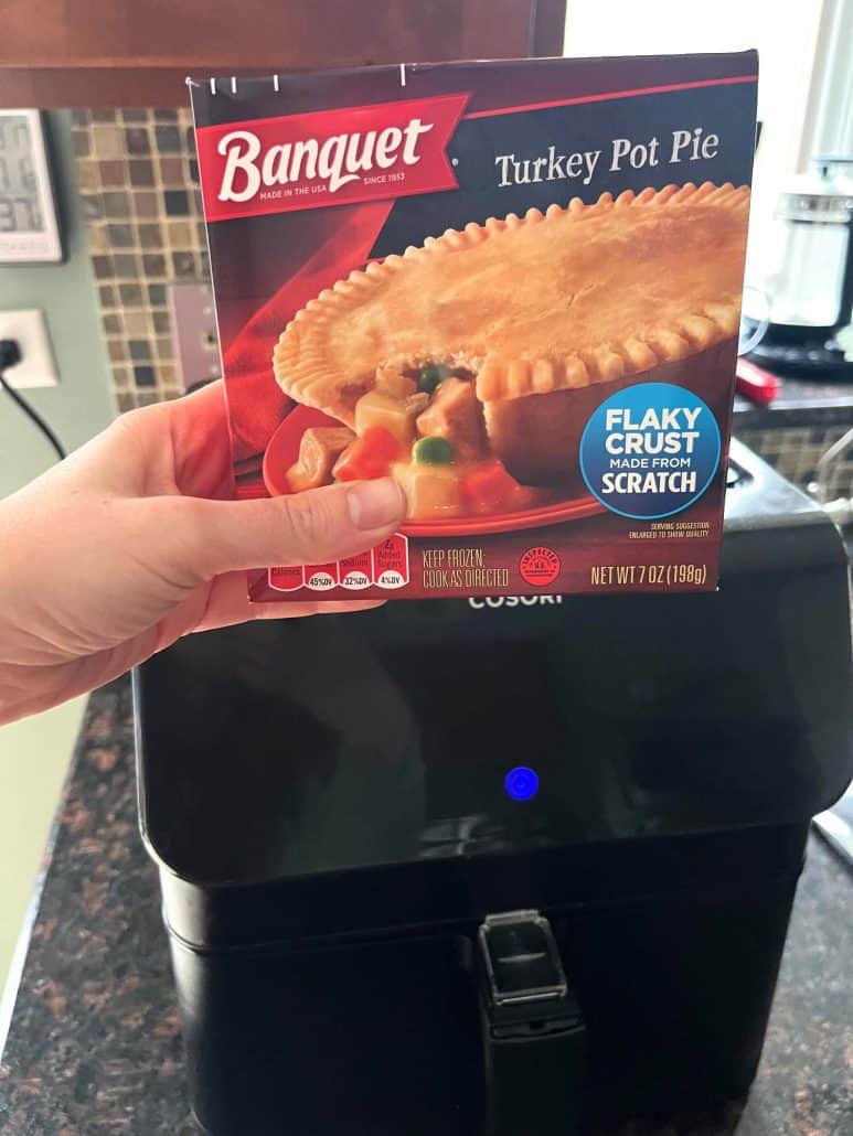 Melanie Mendelson from melaniecooks.com holding a Banquet frozen turkey pot pie box in front of an air fryer, ready to cook the pot pie straight from frozen.