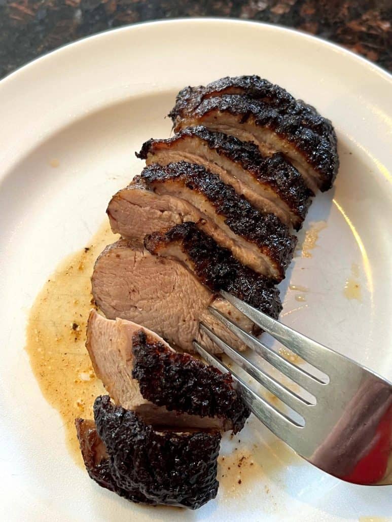 Fork cutting into a slice of juicy air fryer duck breast on a plate, showcasing the tender texture.