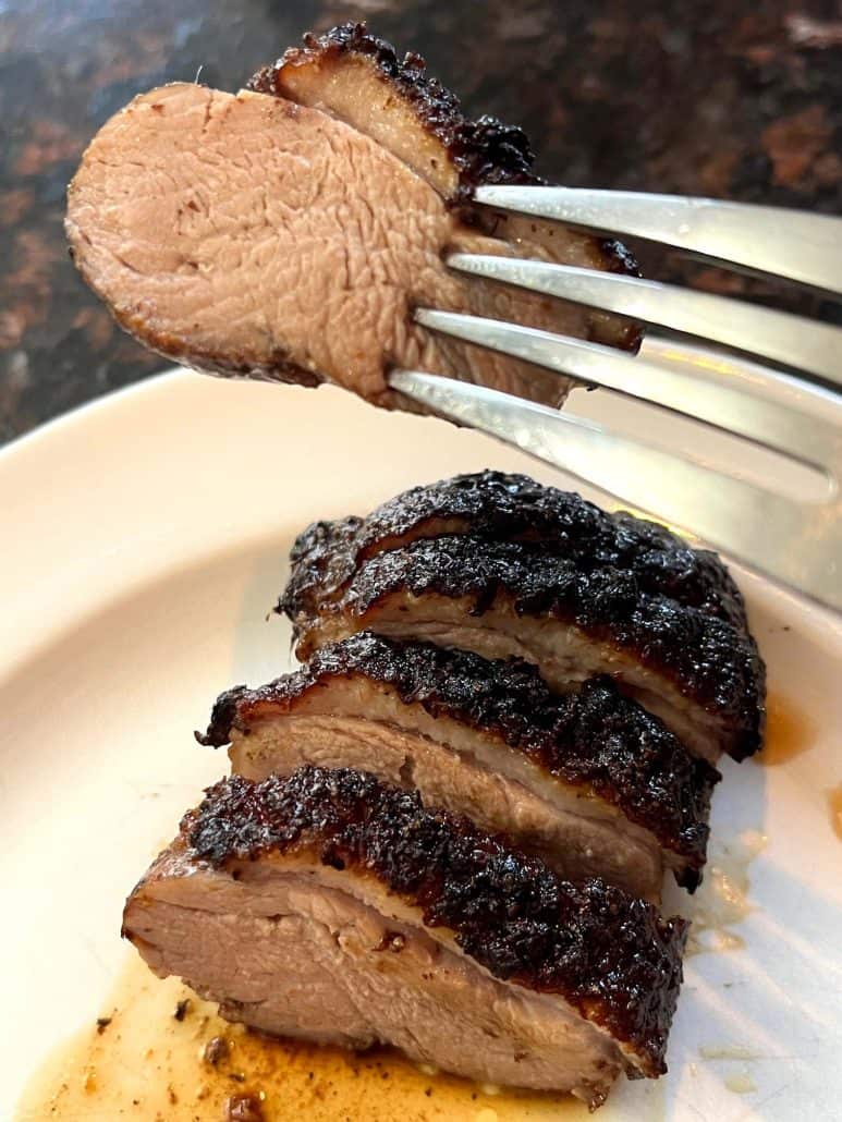 Close-up of a fork holding a bite of sliced air fryer duck breast, showing the juicy interior and crispy browned skin from the finished dish.