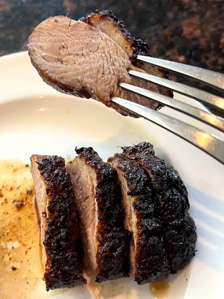 Fork holding a juicy slice of air fryer duck breast above the plate, showing the tender inside and caramelized skin from the finished recipe.