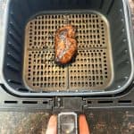 Cooked duck breast in an air fryer basket after 15 minutes at 400°F, showing crispy skin as part of the Air Fryer Duck Breast recipe.