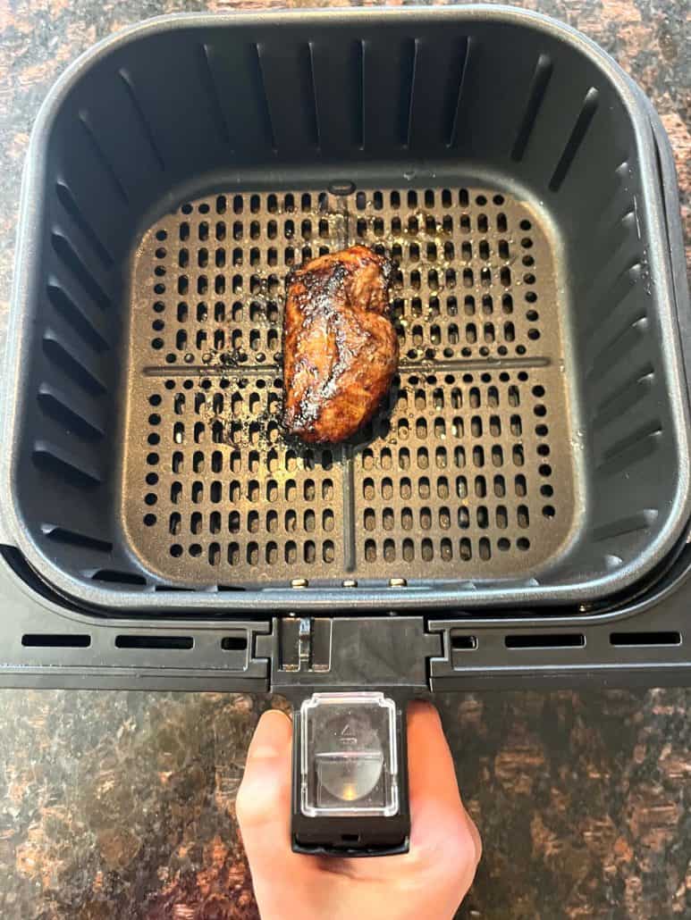 Cooked duck breast in an air fryer basket after 15 minutes at 400°F, showing crispy skin as part of the Air Fryer Duck Breast recipe.