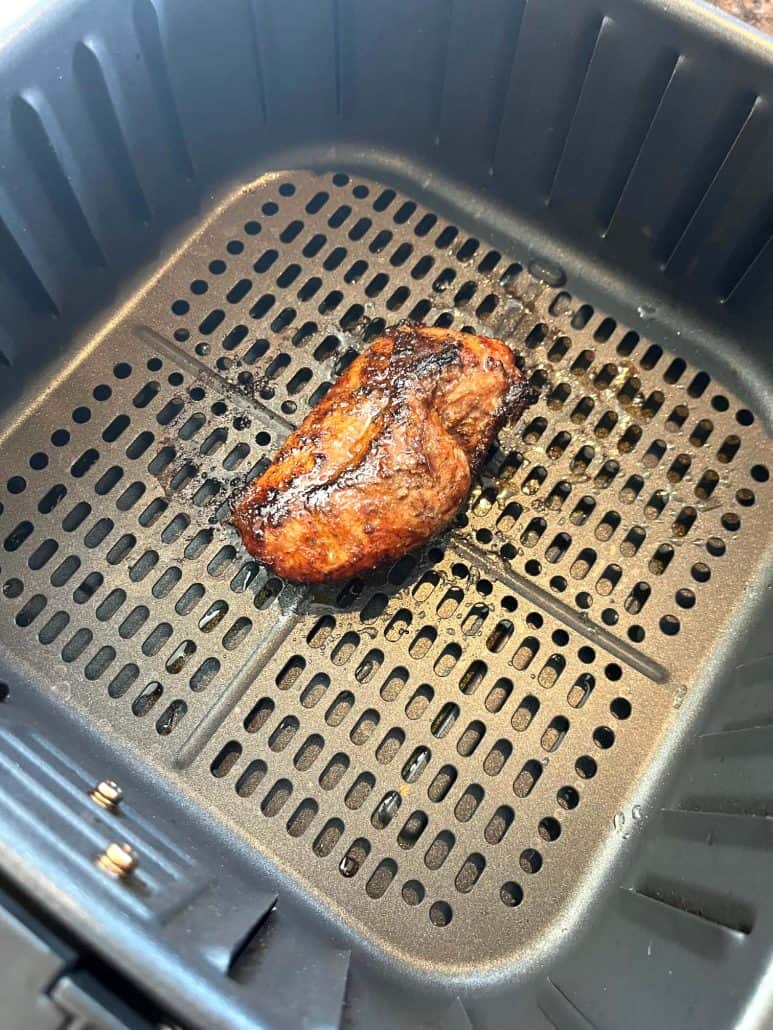 Close-up of crispy, cooked duck breast in an air fryer basket, fresh from the fryer.