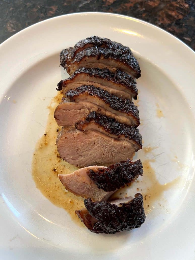 Sliced air fryer duck breast on a white plate, showing juicy, tender meat with crispy skin.