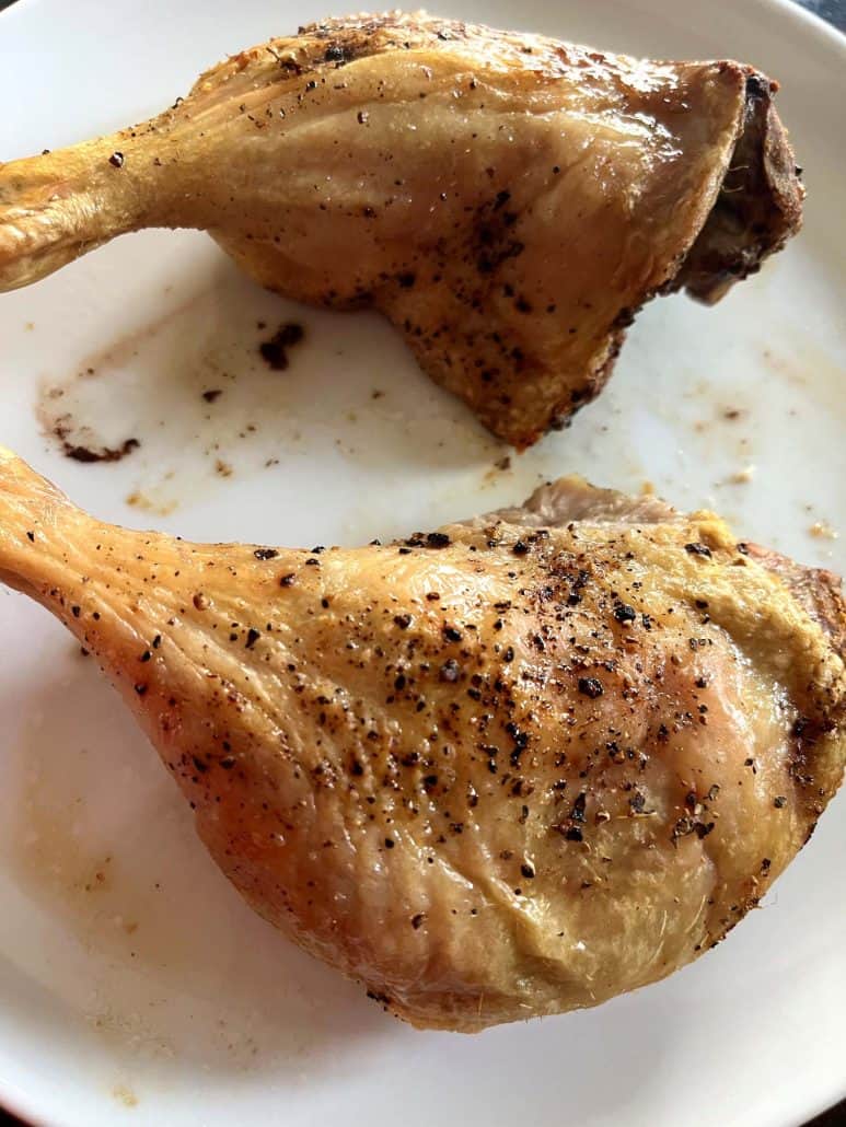 Close-up of two seasoned duck legs on a plate, fresh from the air fryer and ready to serve.