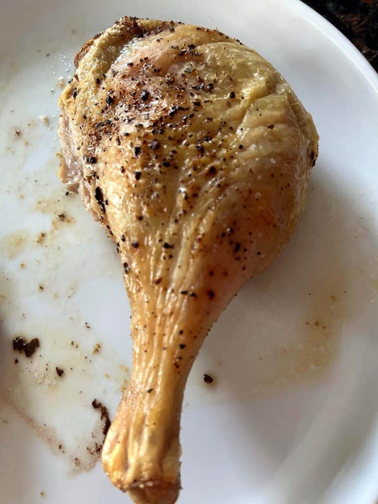 Single crispy duck leg on a white plate, showing the golden brown skin.