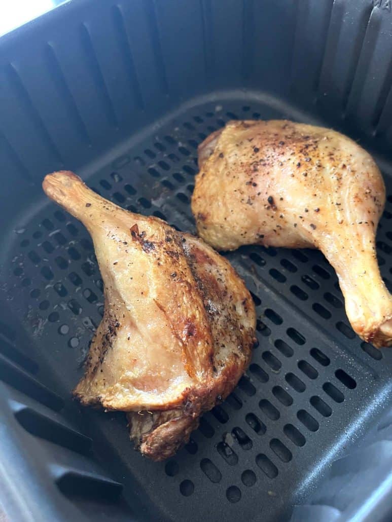 Two perfectly cooked duck legs with crispy skin inside the air fryer basket.