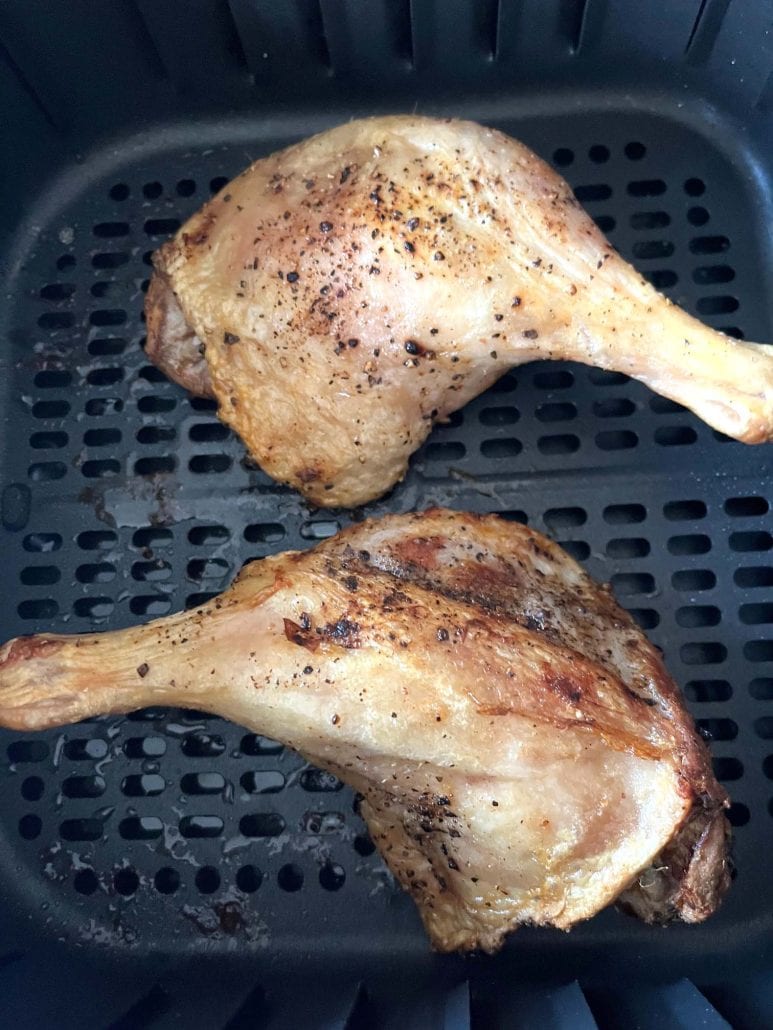 Close-up of two air-fried duck legs with golden, crispy skin inside the air fryer basket, ready to serve.