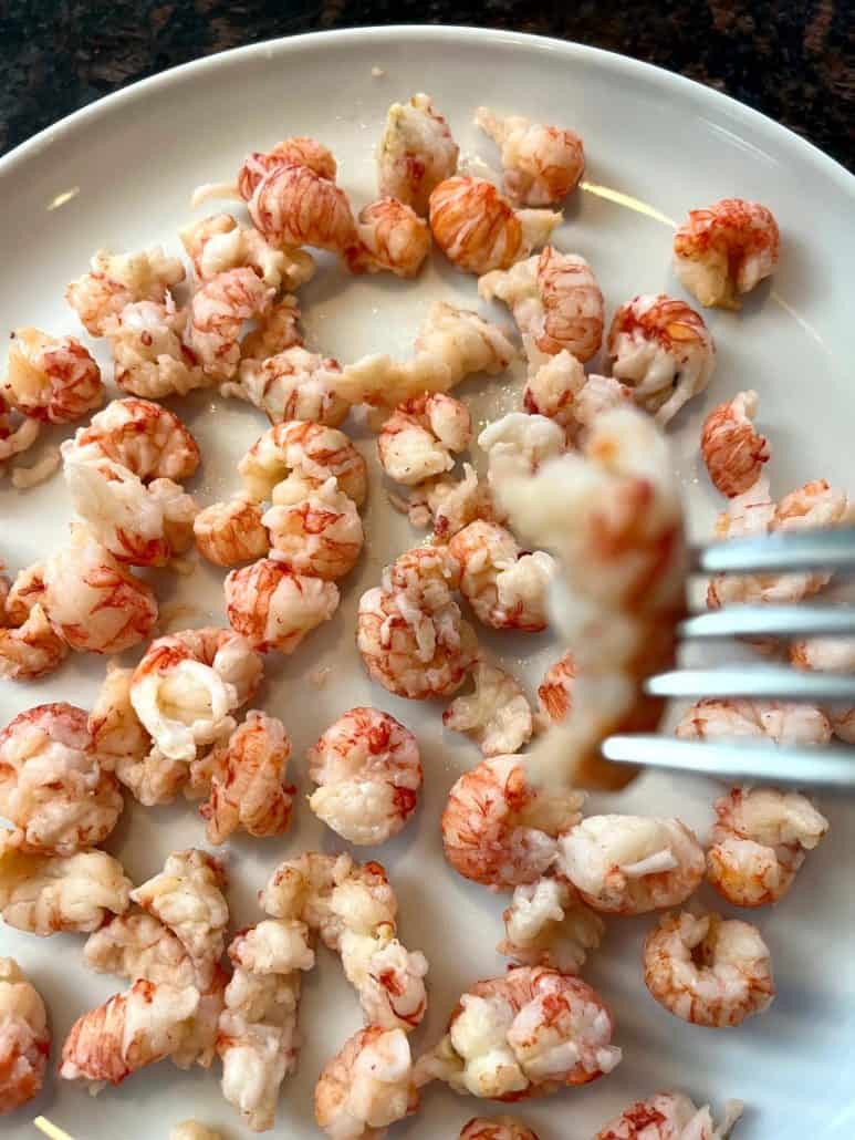 A fork picking up a piece of frozen langostino tail from a plate, ready for a quick and tasty seafood meal.
