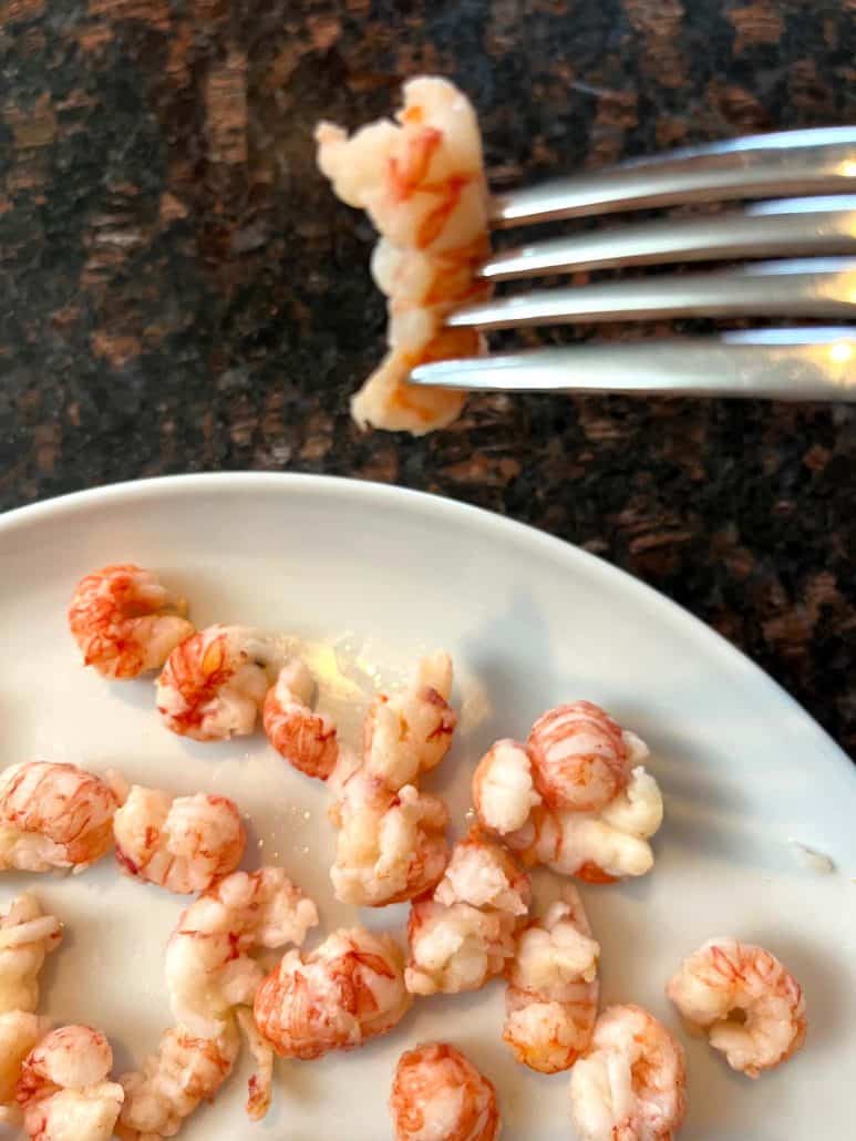 Melanie Mendelson from melaniecooks.com holding a fork, lifting a cooked langostino tail above a plate, ready to enjoy.