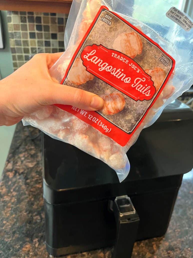Melanie Mendelson from melaniecooks.com holding a bag of frozen Trader Joe’s langostino tails over an air fryer, ready to cook them straight from frozen.