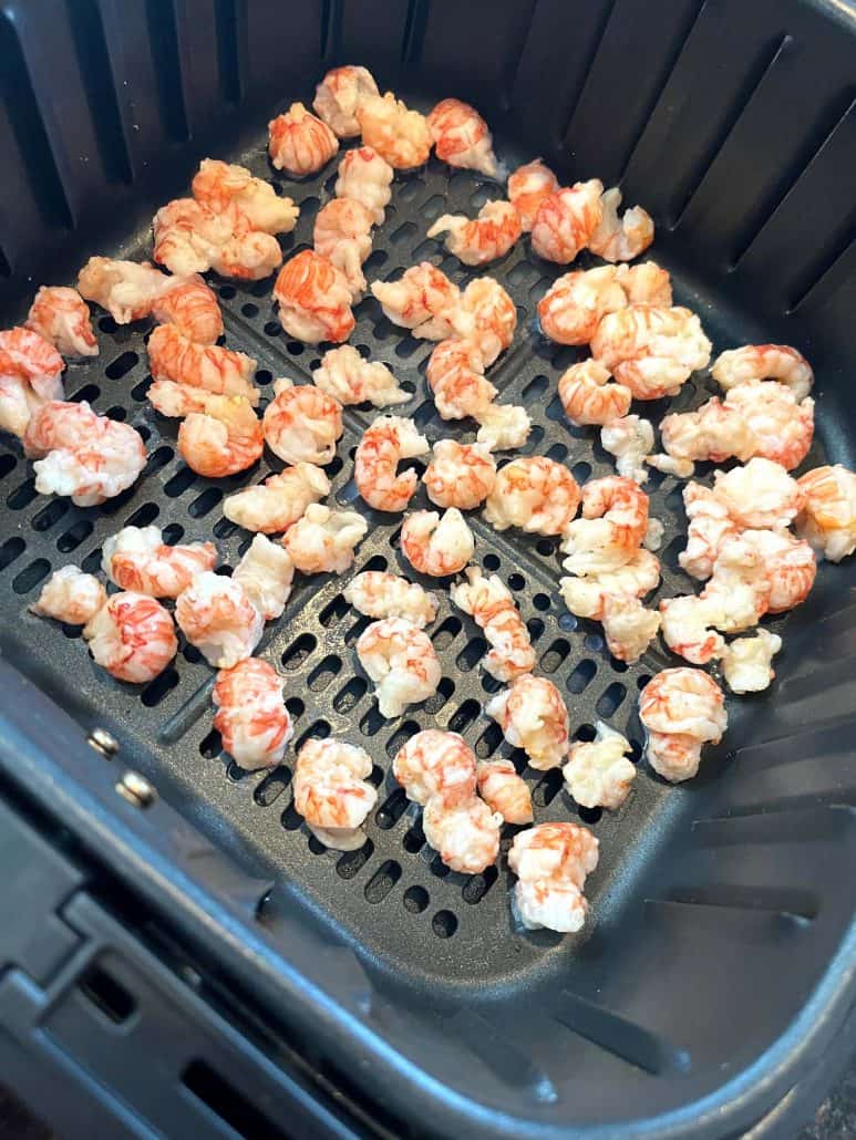 Frozen langostino tails placed in an air fryer basket, ready to be cooked for a quick and easy seafood dish.