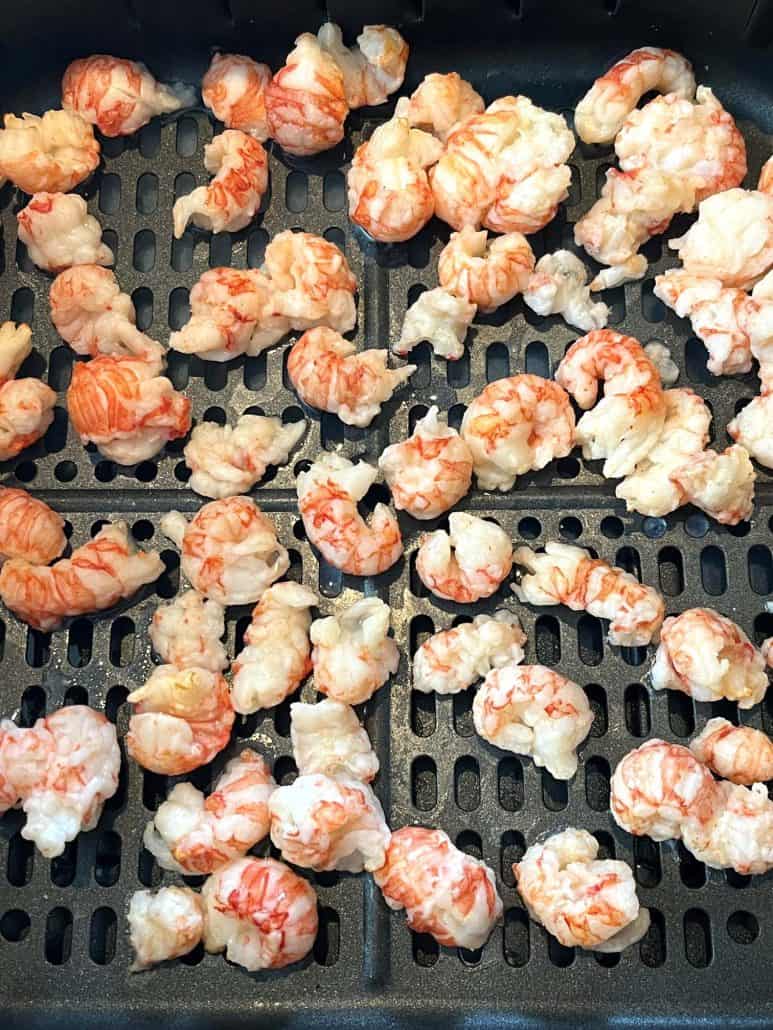 Frozen langostino tails arranged in an air fryer basket, ready to be cooked.