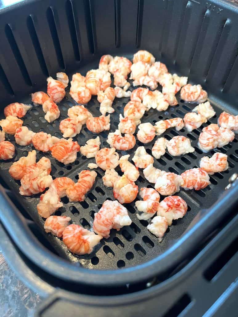 Frozen langostino tails spread in a single layer inside an air fryer basket, ready to be cooked to perfection.