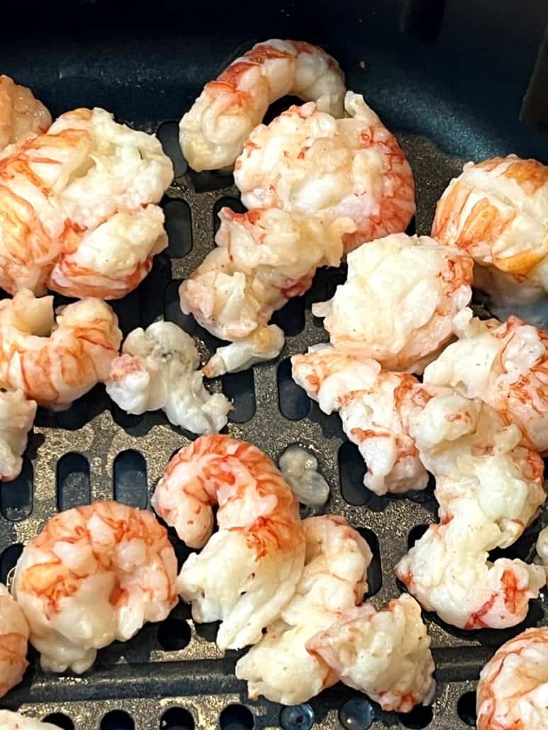 Close-up of frozen langostino tails in an air fryer basket, showing their delicate texture before cooking.