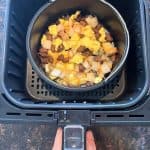 Air fryer basket with a Jimmy Dean breakfast bowl cooking in an oven-safe dish, topped with melted cheese—perfectly cooked using the air fryer.
