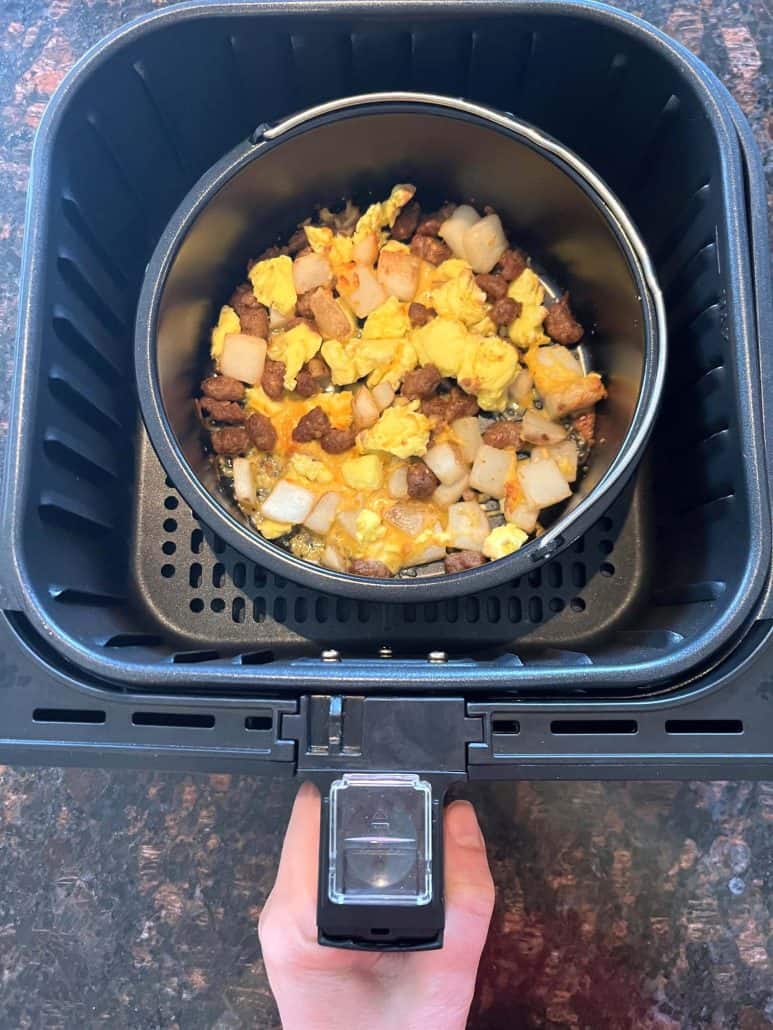 Air fryer basket with a Jimmy Dean breakfast bowl cooking in an oven-safe dish, topped with melted cheese—perfectly cooked using the air fryer.