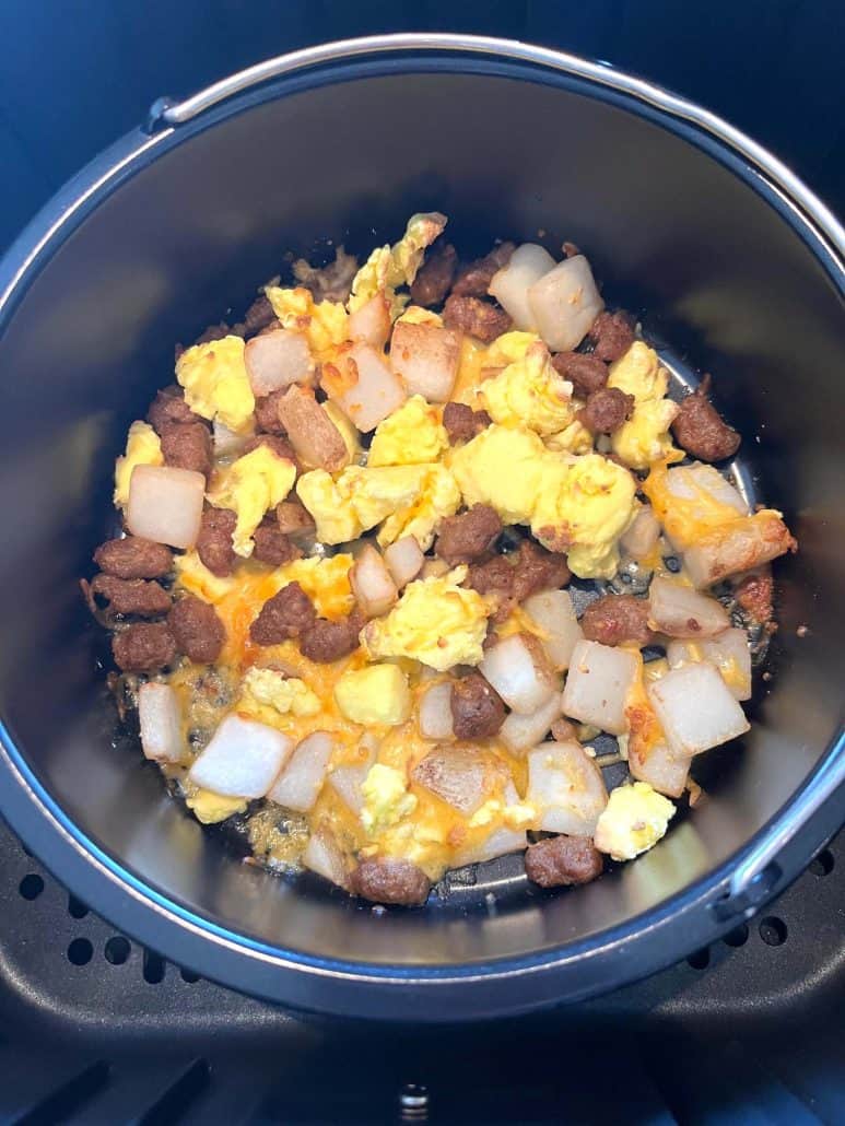 Overhead view of a cooked Jimmy Dean breakfast bowl in an air fryer-safe dish, showing melted cheese, eggs, potatoes, and sausage.