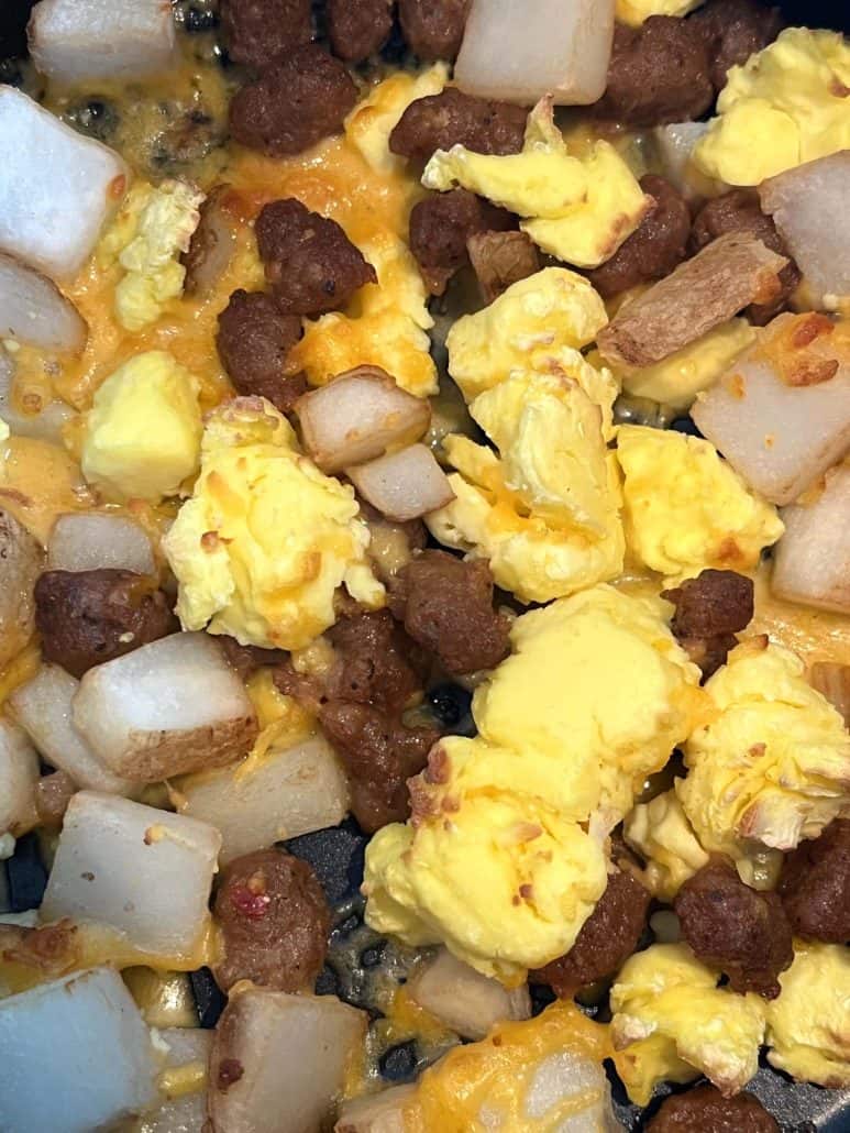 Extreme close-up of cooked Jimmy Dean breakfast bowl showing scrambled eggs, sausage, potatoes, and melted cheese—highlighting the texture and doneness after air frying.