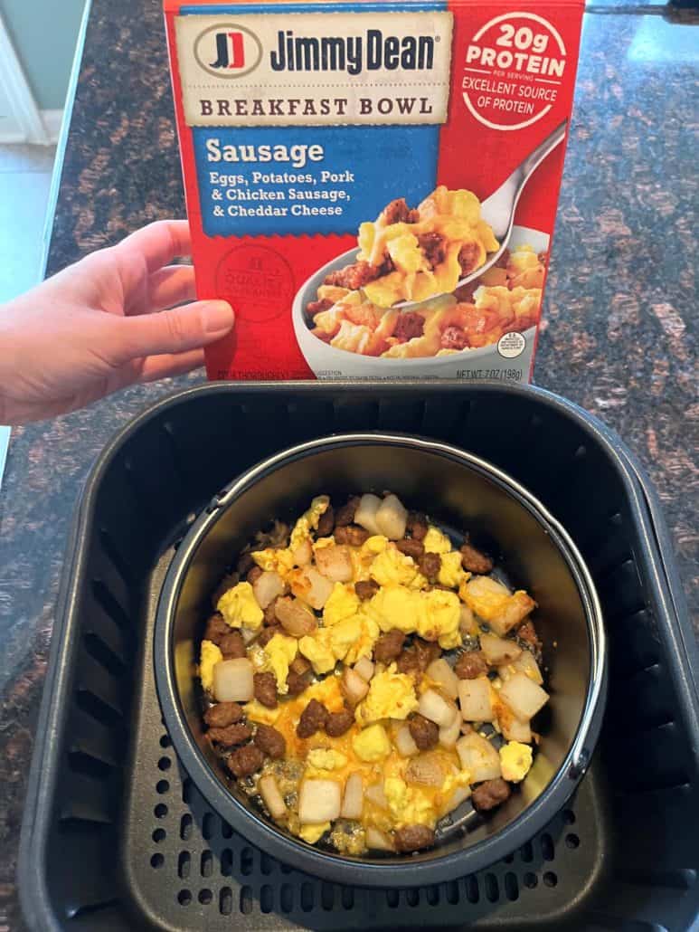 Melanie Mendelson from melaniecooks.com, holding a Jimmy Dean Breakfast Bowl box above an air fryer basket filled with the cooked breakfast bowl.