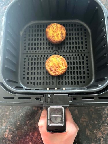 Two Jimmy Dean frittatas cooking in an air fryer basket, showing how to easily heat them from frozen for a quick breakfast.