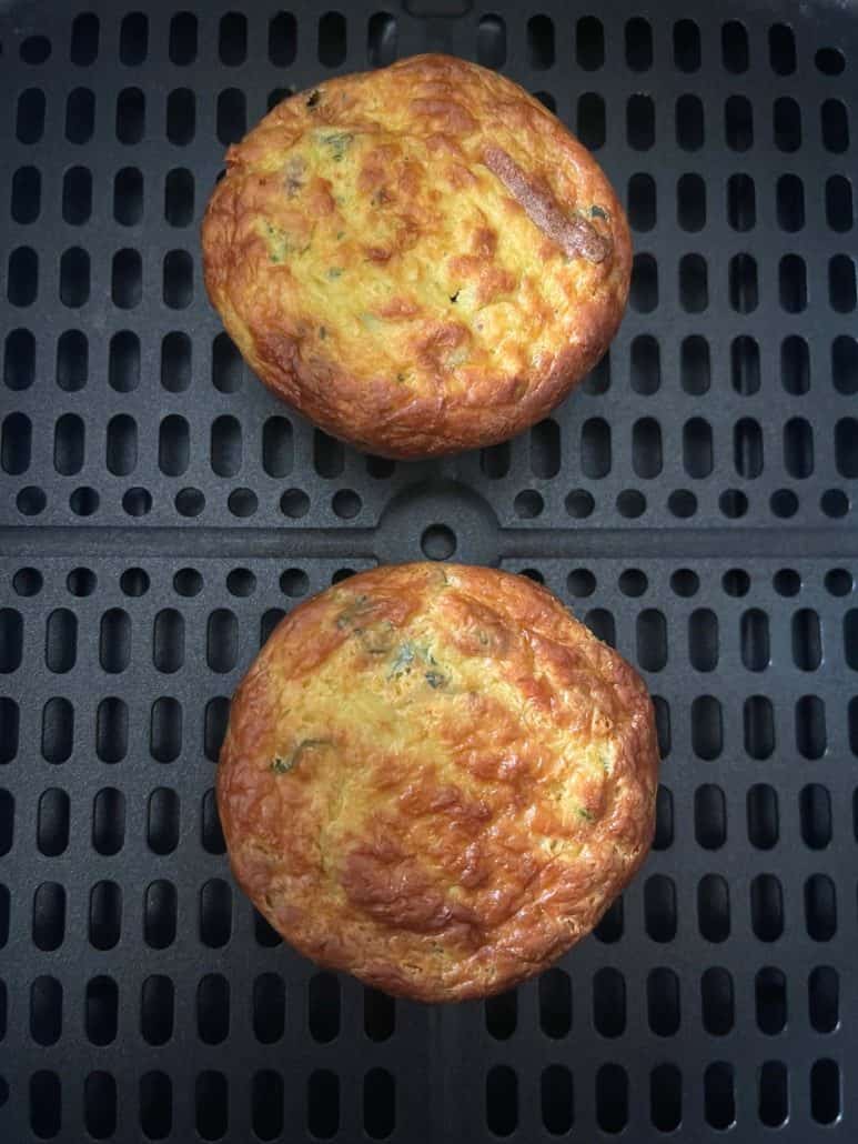 Close-up of two golden brown Jimmy Dean frittatas in the air fryer basket, showing how perfectly they cook using the air fryer method.