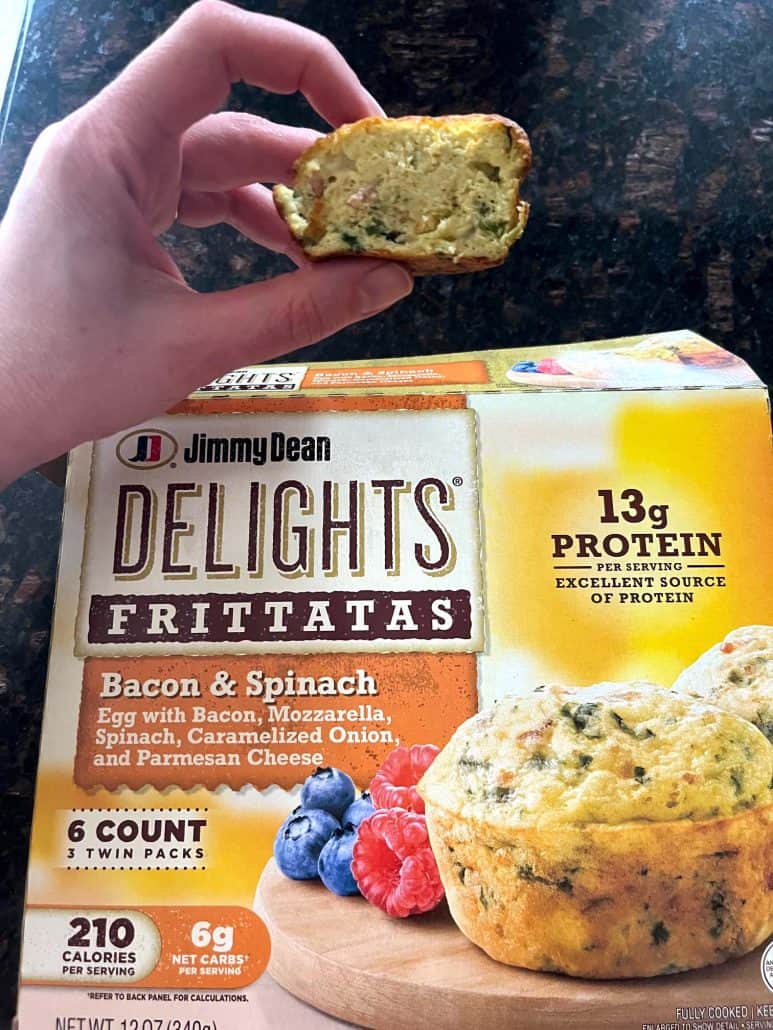 Hand of Melanie Mendelson from melaniecooks.com holding a sliced Jimmy Dean Bacon & Spinach Frittata to show the cooked inside, with the product box in the background.