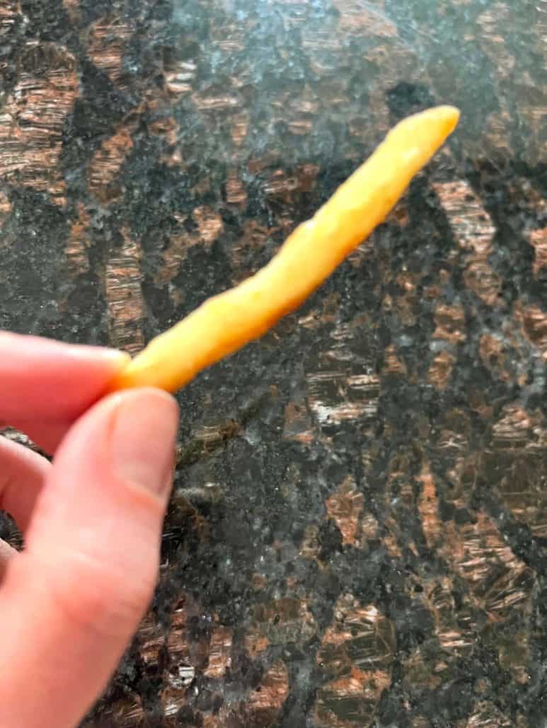 Melanie Mendelson from melaniecooks.com holding a single crispy McCain Beer Battered Fry, showing its golden brown texture from the Air Fryer McCain Beer Battered Fries recipe.