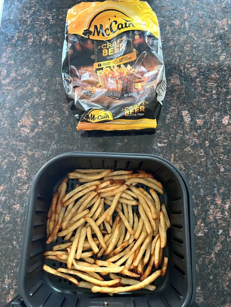 Cooked McCain Beer Battered Fries in an air fryer basket with the empty fries bag in the background.