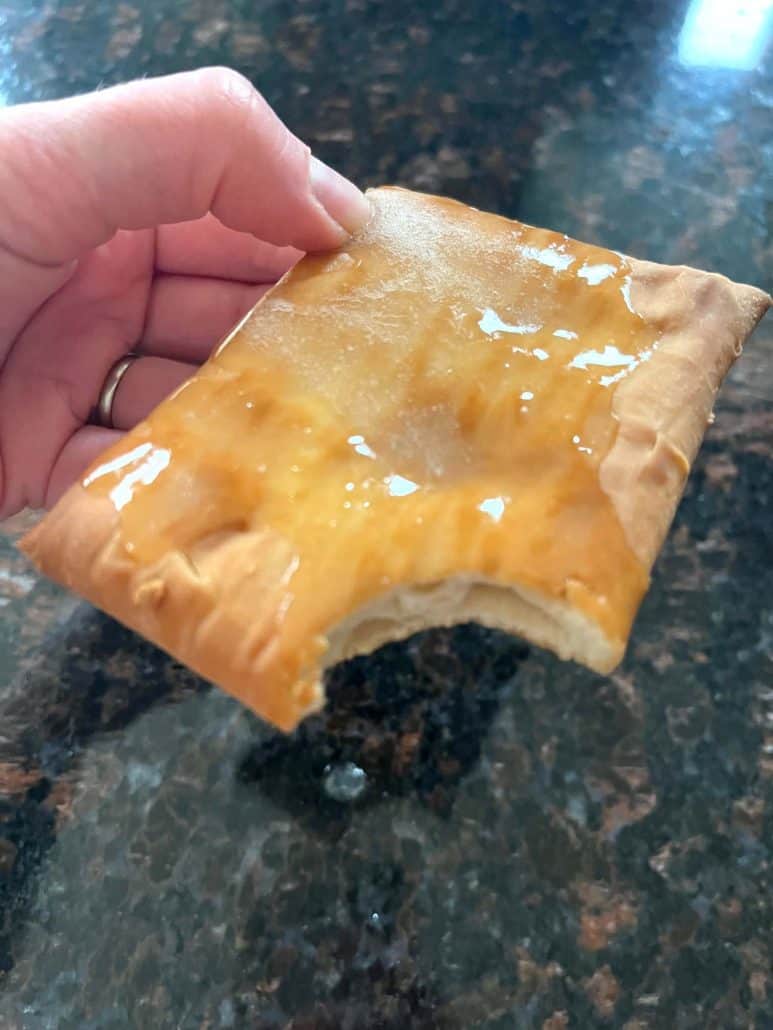 Hand of Melanie Mendelson from melaniecooks.com holding a frosted Pillsbury Toaster Donut Pastry with a bite taken out, showing the crispy outside and soft inside of this easy air fryer pastry.