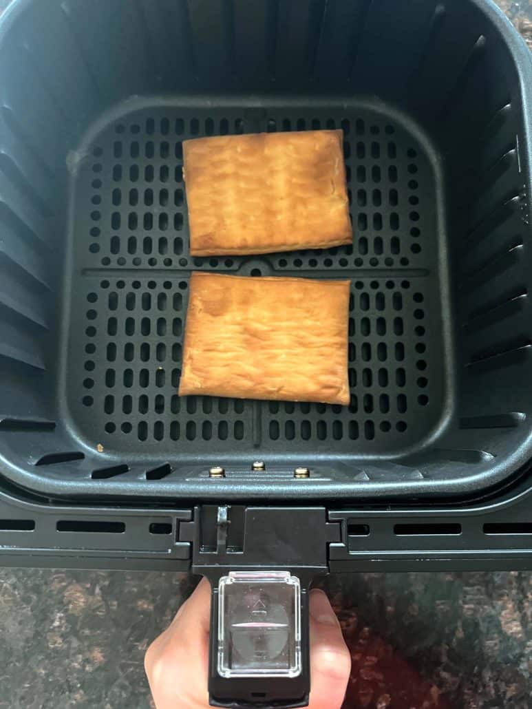Two Pillsbury toaster pastries cooked in an air fryer basket, showing how they look perfectly browned and ready to frost. 
