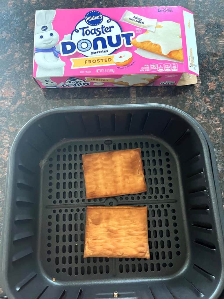 Two Pillsbury Toaster Donut Pastries cooked in an air fryer basket with the product box in the background, showing the finished result.