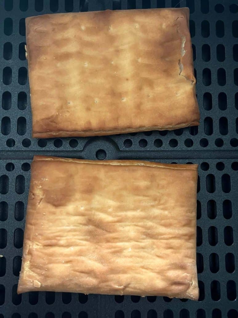 Close-up of two golden brown Pillsbury Toaster Donut Pastries in an air fryer basket, showing their crispy texture right after cooking.