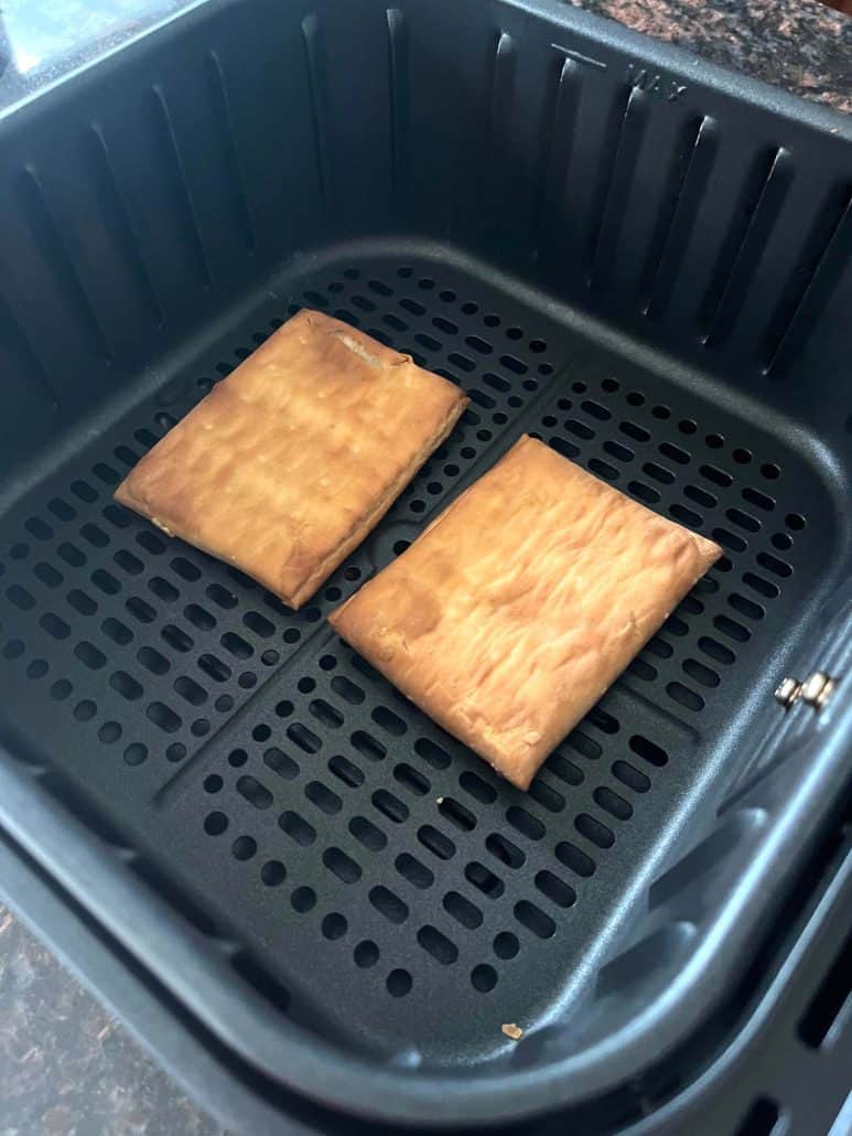 Two golden brown Pillsbury Toaster Donut Pastries sitting in an air fryer basket, freshly cooked.