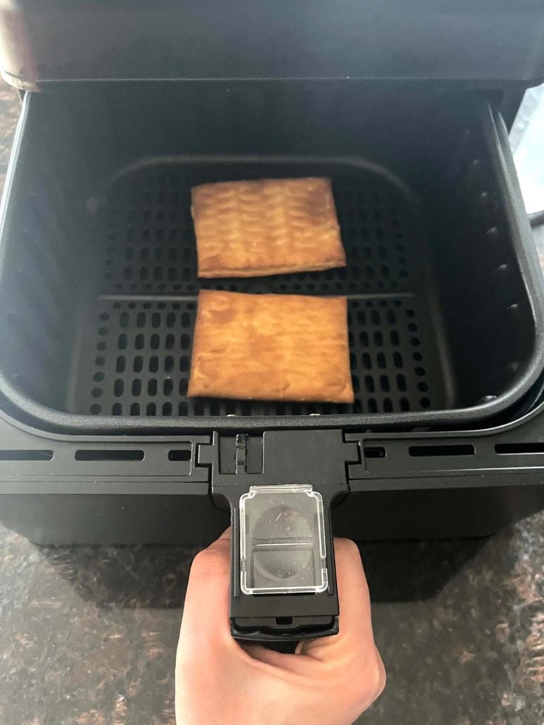Two Pillsbury toaster donut pastries freshly cooked in an air fryer basket, showing how they look perfectly browned.