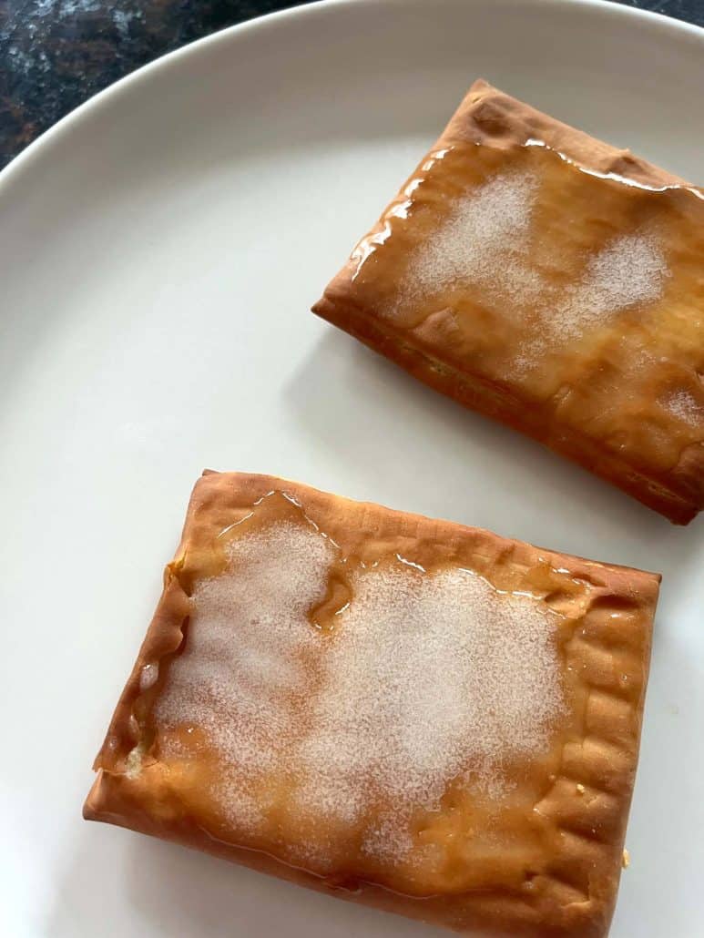 Two frosted Pillsbury Toaster Donut Pastries on a white plate, freshly cooked and ready to enjoy as a quick air fryer dessert or snack.