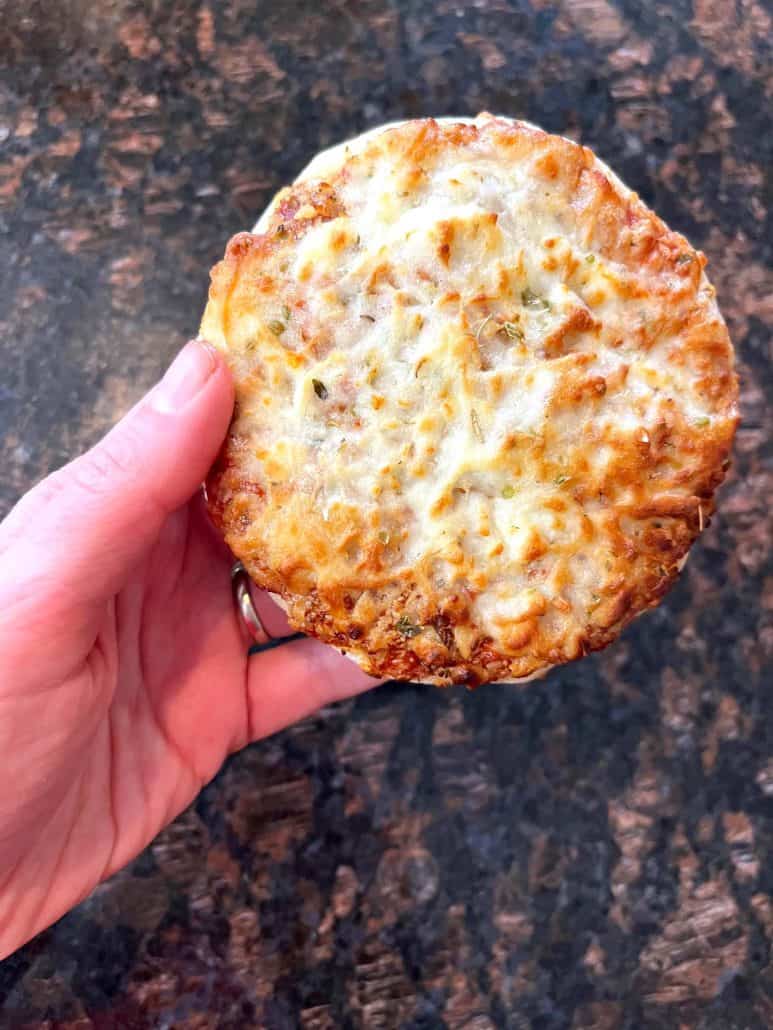 Melanie Mendelson from melaniecooks.com holding a crispy, golden-brown Trader Joe’s Bambino Pizza, showing the perfect air fryer result ready to eat.