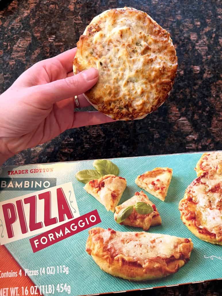 Melanie Mendelson from melaniecooks.com holding a cooked Trader Joe’s Bambino Pizza above the product box, showing the air-fried mini pizza next to its packaging.
