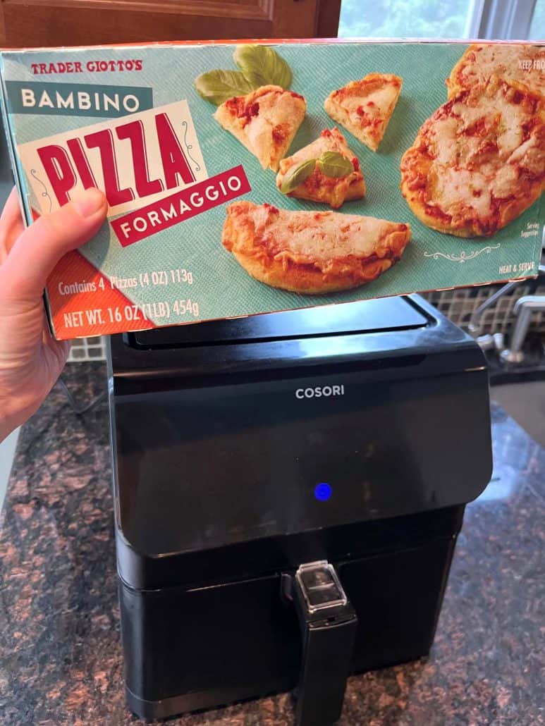 Melanie Mendelson from melaniecooks.com holding a box of Trader Joe’s Bambino Pepperoni Pizzas in front of an air fryer, showing the product used for the quick air fryer mini pizza recipe.