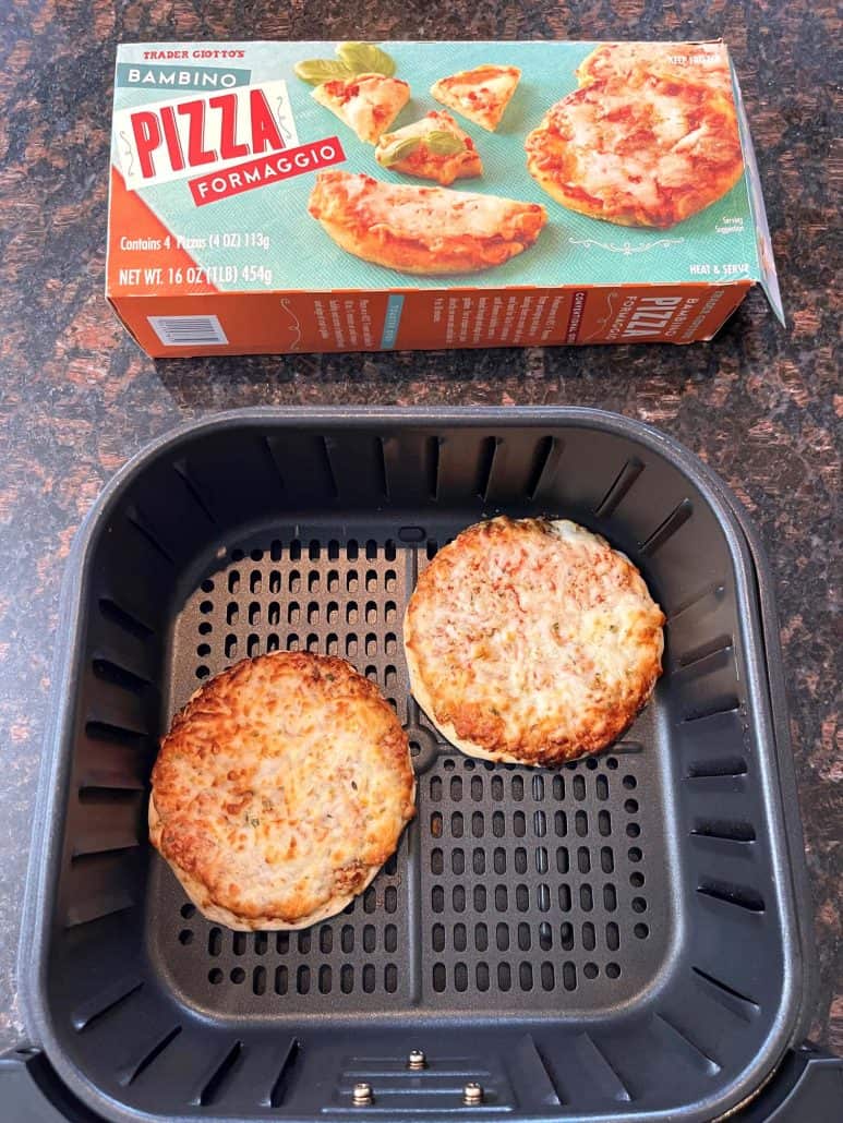 Two cooked Trader Joe’s Bambino Pizzas in an air fryer basket with the pizza box in the background, showing the final result.